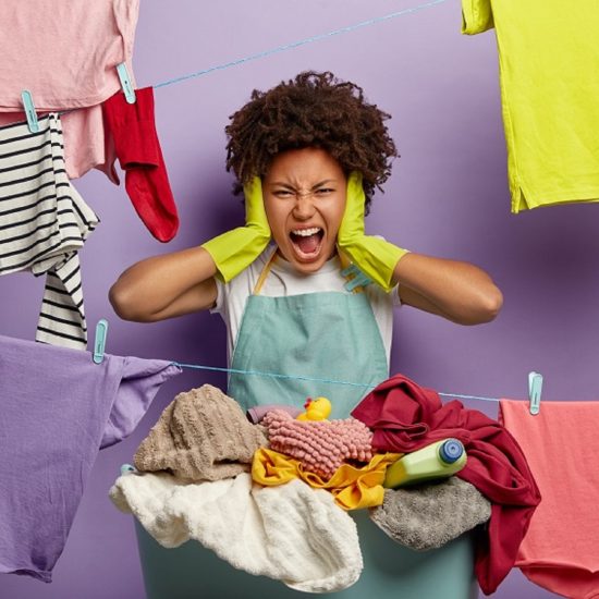 Stressful discontent woman feels overworked, shouts from anger, does laundry alone, demands husband to help, stands near clotheslines with hanged linen, wears gloves and apron. Much housework